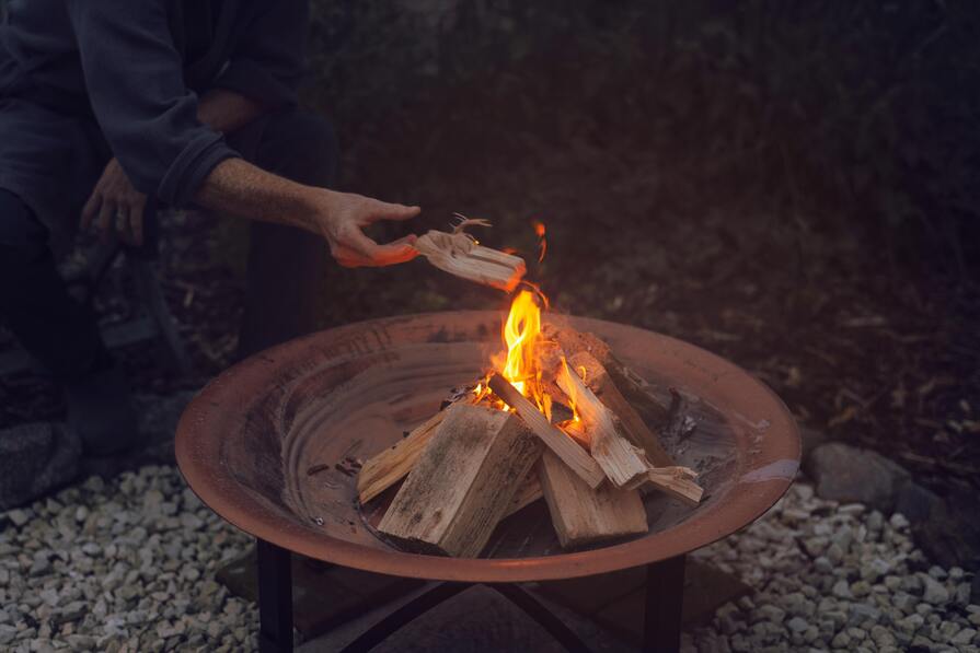 Feuerstelle auf Kiesuntergrund mit Mann der Holz nachlegt